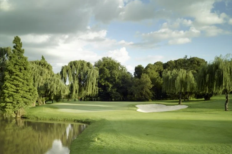 Green del Glendower Golf Club junto a un estanque, un búnker y árboles frondosos.