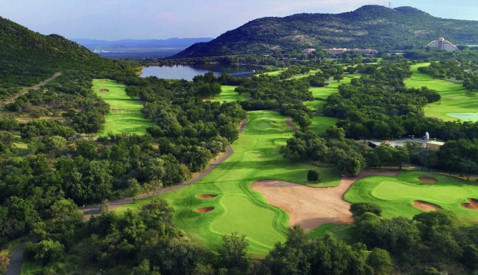 Vista panorámica del Gary Player Country Club con calles verdes, búnkeres, un lago y montañas.
