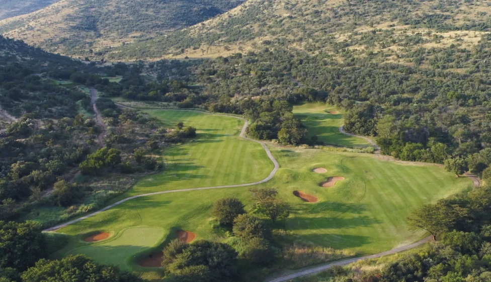 Vista aérea del Lost City Golf Club con calles verdes, búnkeres y montañas alrededor.