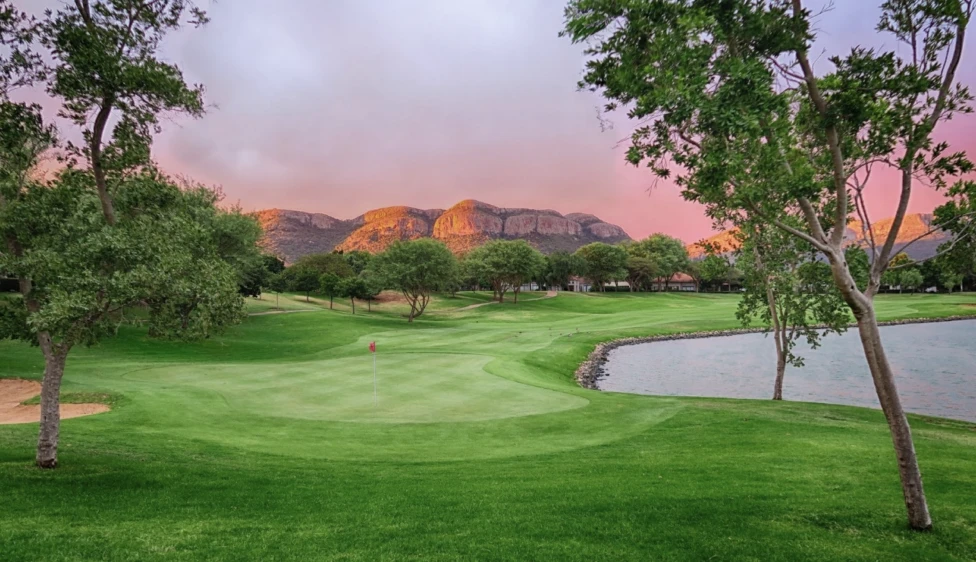 Pecanwood Country Club Green del Pecanwood Country Club junto a un lago, con árboles y montañas iluminadas por el atardecer.