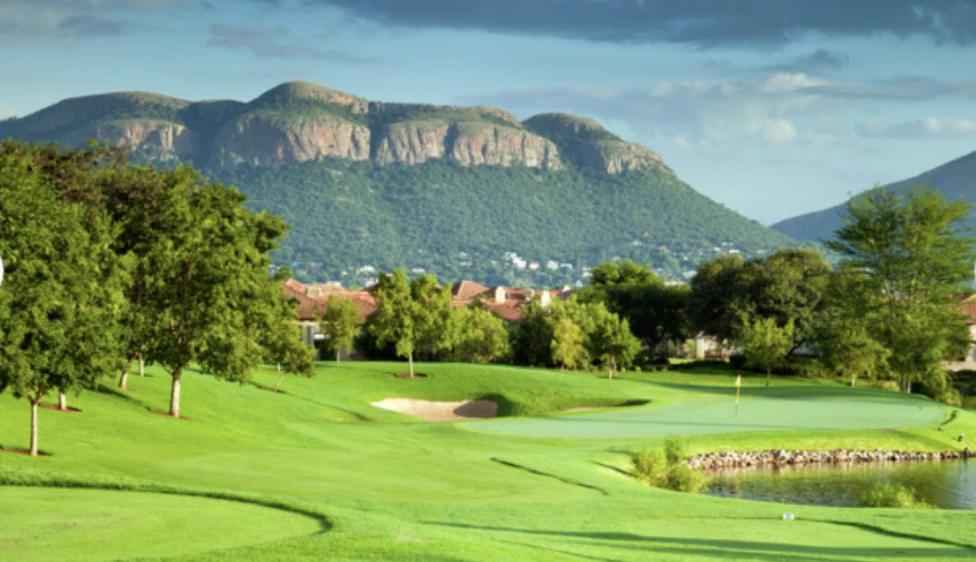 Pecanwood Country Club Green del Pecanwood Country Club junto a un lago, con un búnker, árboles y montañas al fondo.