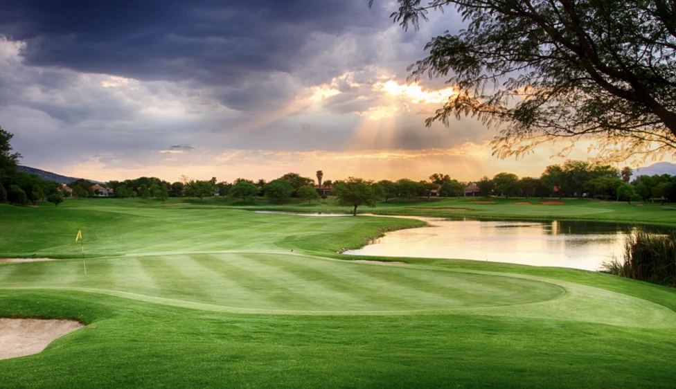 Green del Pecanwood Country Club junto a un lago y un búnker bajo la luz del atardecer.