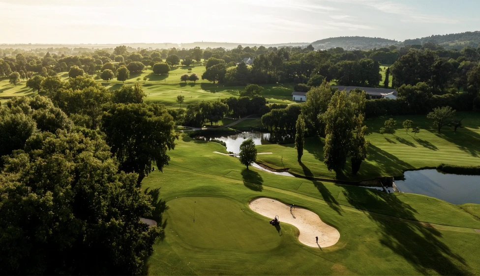 Green del Royal Johannesburg Country Club junto a búnkeres, lagos y árboles bajo luz cálida.
